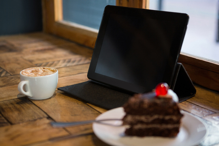 Digital tablet with pastry and coffee cup on table in cafeの写真素材