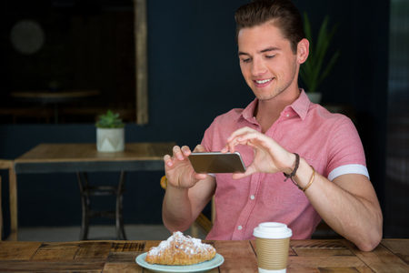 Happy young man photographing food on table in coffee shopの写真素材
