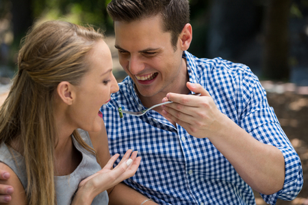 Smiling young man feeding woman at outdoor restaurantの写真素材