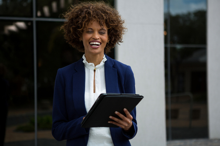 Smiling businesswoman using digital tablet near office buildingの写真素材