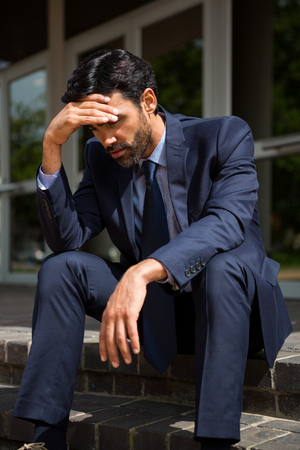 Stressed businessman sitting on steps in conference centreの写真素材