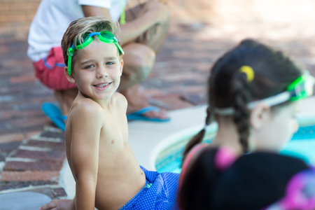 Portrait of little boy sitting with friends at poolsideの写真素材
