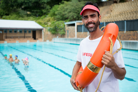 Portrait of lifeguard standing with lifebuoy near poolsideの写真素材