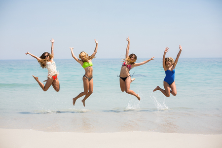 Female friends in bikinis jumping on shore at beachの写真素材