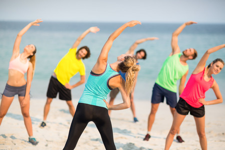 Friends stretching while standing on shore at beachの写真素材