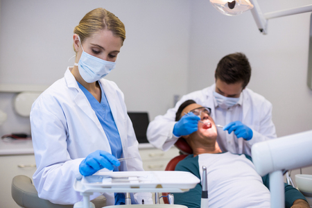 Dentist holding dental tool while his colleague examining patient in background at clinicの写真素材