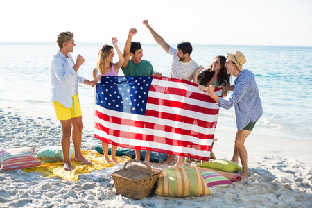 Happy friends holding American flag on shore at beachの写真素材