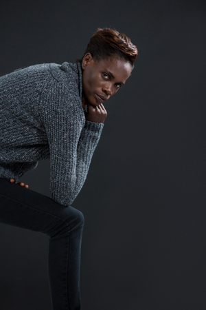 Androgynous man posing with hand on his chin against grey backgroundの写真素材
