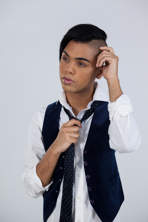 Thoughtful transgender young female with head in hand standing against white backgroundの写真素材