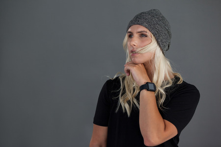 Thoughtful transgender woman wearing knit hat gray background