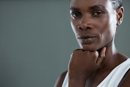Androgynous man posing with hand on chin against grey backgroundの写真素材