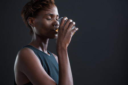 Androgynous man drinking whiskey from glass against grey backgroundの写真素材