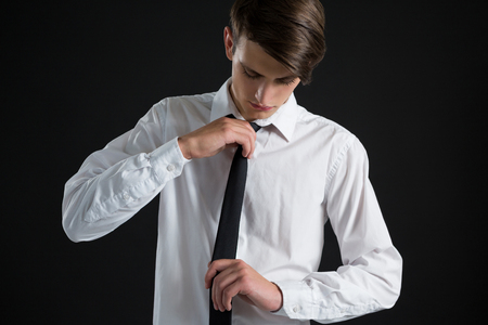 Androgynous man adjusting his tie against black backgroundの写真素材
