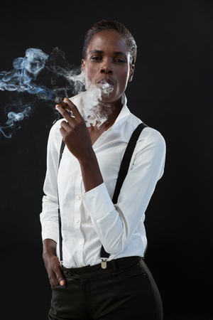 Androgynous man smoking a cigar against grey backgroundの写真素材
