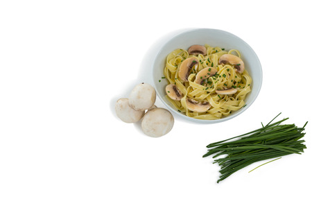 Pasta served in bowl by mushrooms and scallion against white backgroundの写真素材