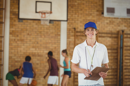 portrait of coach smiling at camera while high school team playing basketball in backgroundの写真素材
