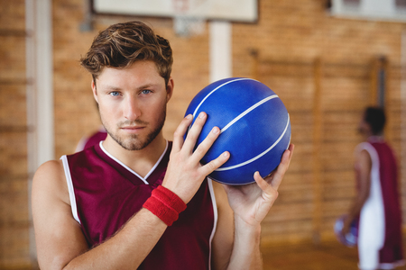 Portrait of confident basketball player holding basketball in the courtの写真素材