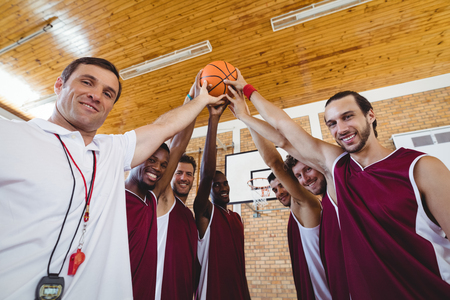 Portrait of smiling players and coach holding basketball together in the courtの写真素材