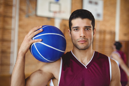 Portrait of confident basketball player holding a basketball in the courtの写真素材