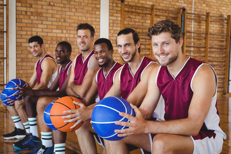 Portrait of smiling basketball players sitting on bench with basketball in the courtの写真素材