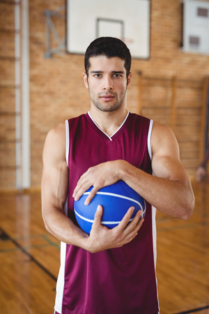 Portrait of determined basketball player holding a basketball in the courtの写真素材