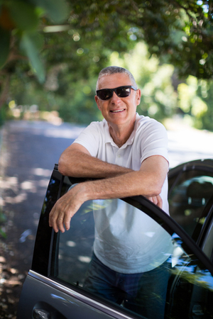 Portrait of smiling senior man leaning on car doorの写真素材