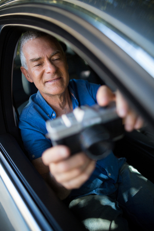 Smiling senior man taking selfie with camera while sitting in carの写真素材