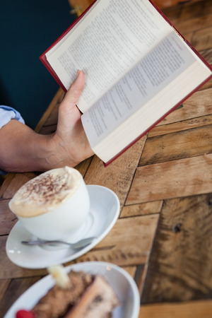 Cropped image of senior woman reading book while sitting by coffee cup at table in cafe shopの写真素材