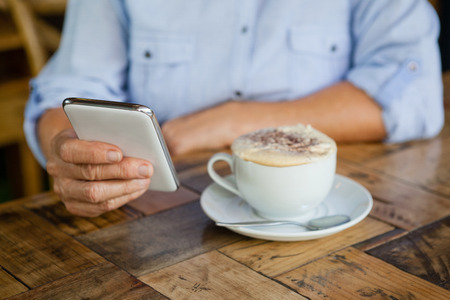Cropped image of person holding smart phone while sitting by coffee cup at table in cafeの写真素材