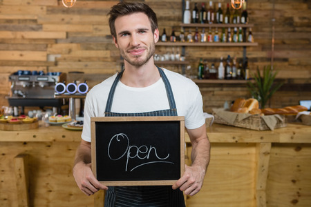 Portrait of smiling waiter standing with open signboard at counter in counterの写真素材