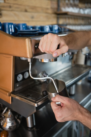 Close-up of waiter hands pouring milk in jug from coffee machine in cafÃ©の写真素材