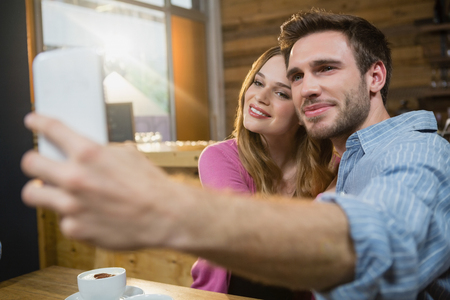 Young couple taking selfie on mobile phone while having coffee in cafÃ©の写真素材