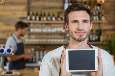 Portrait of smiling waiter showing digital tablet at counter in cafeの写真素材