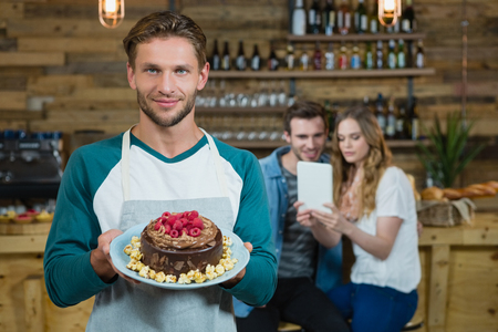 Portrait of waiter holding plate of cake and customer in background in cafeの写真素材
