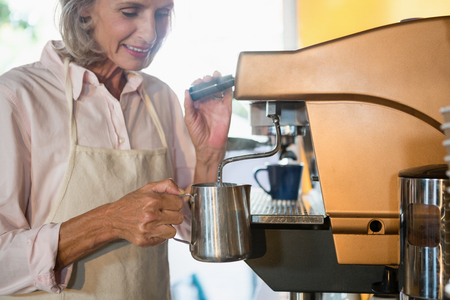 Senior waitress using coffeemaker in cafÃ©の写真素材