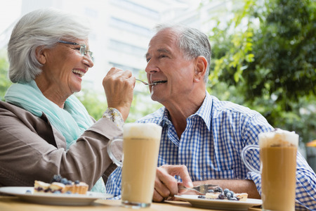 Smiling senior woman feeding tart to man in outdoor caféの写真素材