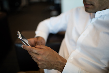 Mid section of businessman using mobile phone while sitting on sofa at officeの写真素材