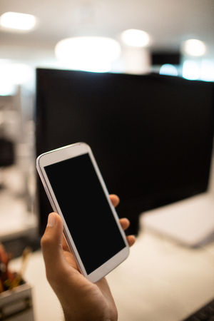 Cropped hand of businessman holding mobile phone in officeの写真素材