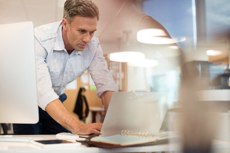 Businessman working on laptop while leaning at desk in officeの写真素材