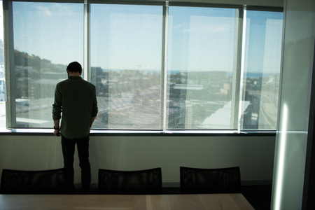 Rear view of businessman standing by window in meeting room at workplaceの写真素材