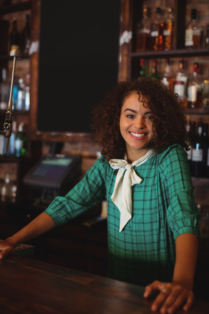 Portrait of beautiful female bar tender standing at bar counterの写真素材