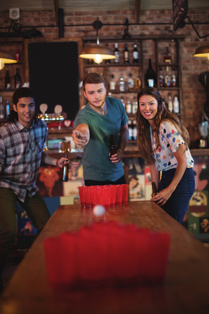 Group of happy friends playing beer pong game in pub