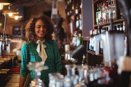 Portrait of beautiful female bar tender standing at bar counterの写真素材