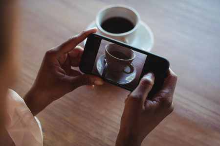 Hands of woman taking a clicking picture of black coffee in restaurant