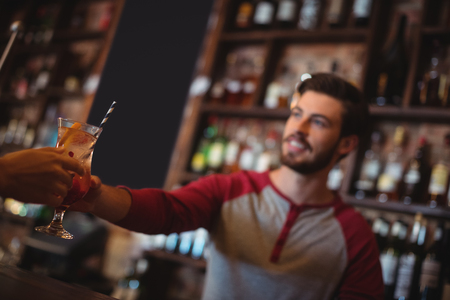 Female bar tender giving glass of cocktail to customer at bar counterの写真素材