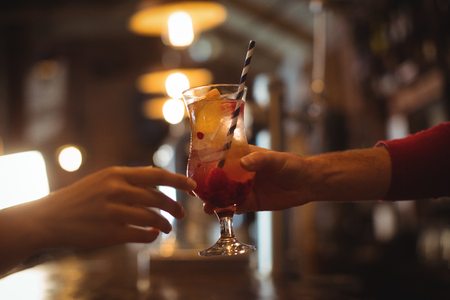 Close-up of female bar tender giving glass of cocktail to customer at bar counterの写真素材