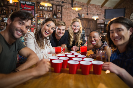 Portrait of smiling friends around disposable cups on table in bar