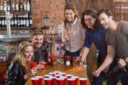 Friends cheering while woman playing beer pong on table in barの写真素材