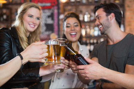 Happy friends toasting beer mugs and bottles in barの写真素材