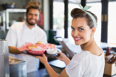 Portrait of smiling waitress taking plate from chef in kitchenの写真素材